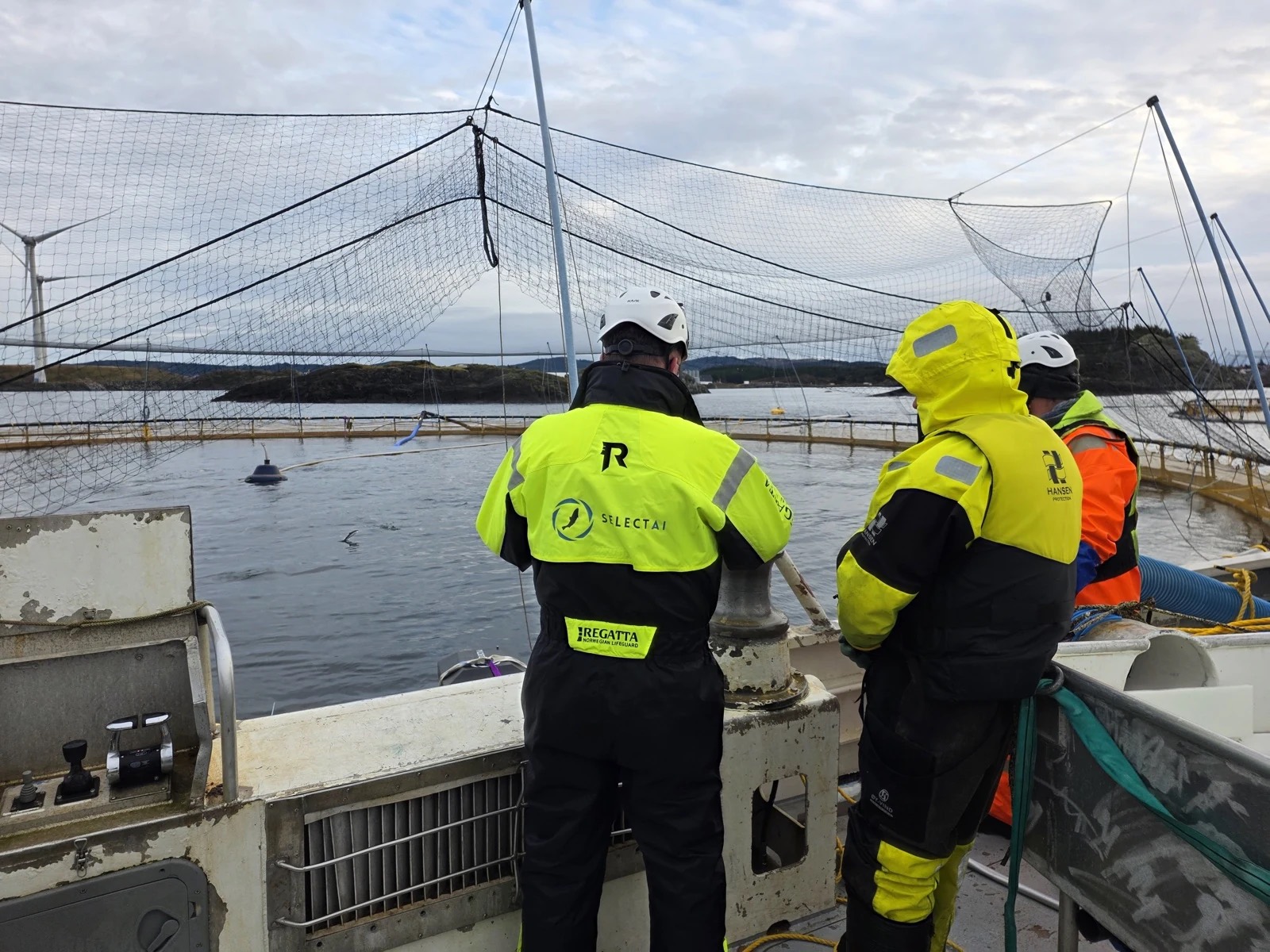 Fish farm workers in SelectAI jackets on a boat beside a salmon pen
